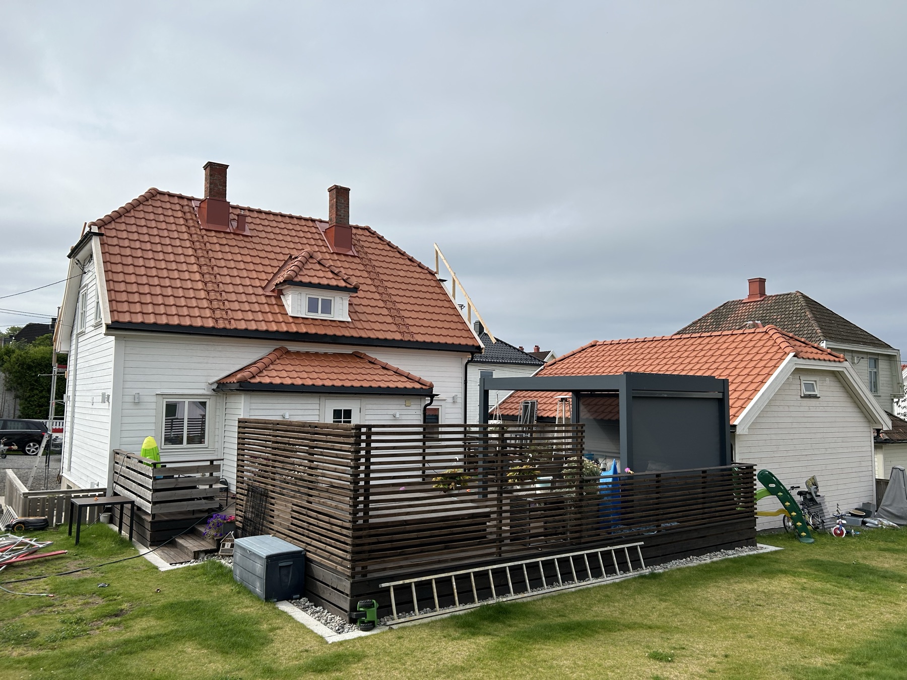 Baksiden av den hvite boligen med nytt teglsteinstak, terrasse og ny garasje